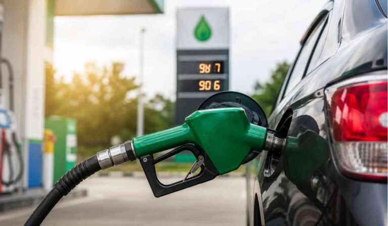 Petrol pump par car me fuel bharte hue green nozzle ka close-up shot, background me fuel prices display board dikh raha hai.