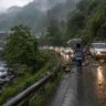 Monsoon Travel Alert से जुड़ी यथार्थवादी तस्वीर, जिसमें पहाड़ी इलाके में भारी बारिश, भूस्खलन से बाधित सड़क और यात्रा कर रहे लोग दिखाई दे रहे हैं।